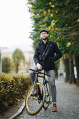 Charming handsome. Young bearded man looking at camera while standing with bicycle in the street