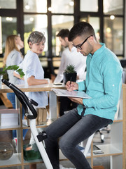 Young businessman sitting on a training bicycle and writting