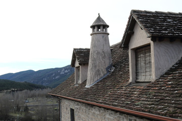 A traditional house dark roof with two mansard windows, round chimney in a Pyrenees mountains village in winter in Hecho, Aragon region, Spain