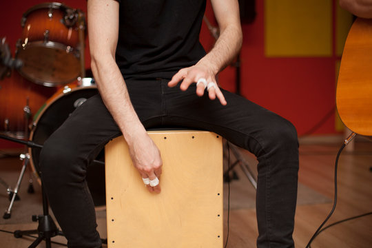 Percussionist playing cajon on a rehearsal studio with drums and music stuff on the background