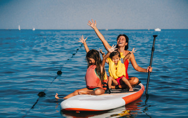 Mother with two daughters stand up on a paddle board - 243741021