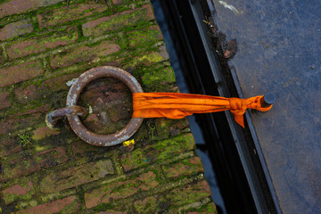 Fototapeta premium Rusty metal ring and boat tied with orange ribbon to the canal shore