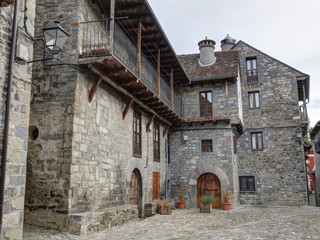 Fototapeta na wymiar A rural landscape of a mountain hamlet with some stone houses with wooden balconies and dark roofs during winter in Ansó, Aragon region, Spain