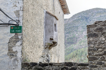 A small protruding window on a stone wall of an old house with Pyrenees mountains on the background in the rural town of Ansó, Aragon, Spain
