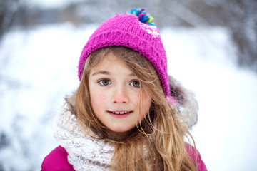 Beautiful young girl wearing pink jacket and knitted hat playing with snow in winter park. Child walking in snowy forest. Family vacation with kid in mountains