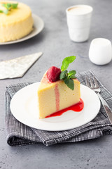 A piece of Japanese cotton cheesecake with mint and strawberry on a white plate. No crust cheesecake. Grey stone or concrete background. Selective focus, copy space. 