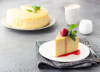 A piece of Japanese cotton cheesecake with mint and strawberry on a white plate. No crust cheesecake. Grey stone or concrete background. Selective focus, copy space.  - obrazy, fototapety, plakaty