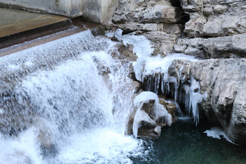 A small waterfall over concrete in the Veral river with grey rock and cold ice stalactites in the Foz de Binies zone, during winter, in Aragon, Spain