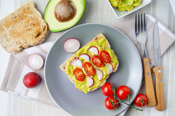 Cenital view of toast with avocado, tomato and radish on a grey plate
