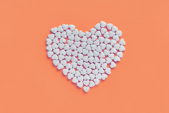 White heart made of heart shaped shugar candies on a living coral pink paper background. Love and health concept.