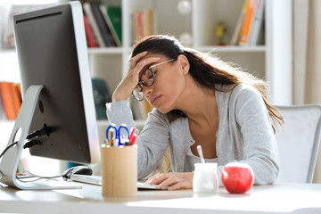 Tired young business woman having headache while working with computer in the office.