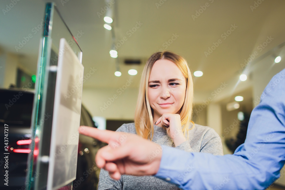 Wall mural Car salesman helps woman client to choose a new car in the dealership.