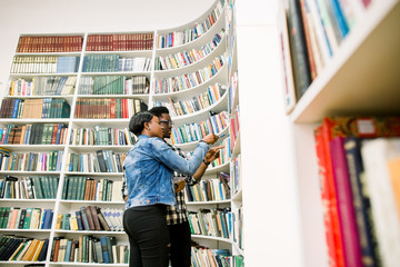 Young college Afro-American students taking book from shelf in library. Handsome young Afro-American man and woman in library.