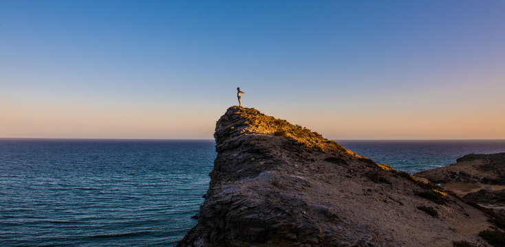 Persona subida en una monta&ntilde;a frente al mar al atardecer 