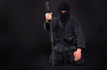 Tired ninja in kimono with katana sits on his lap
