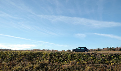 Small gray passenger car stopped on direct countryside road in beautiful autumn landscape panoramic view at eye level in bright sunny day