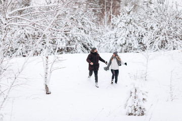 Naklejka na ściany i meble Young couple running on a snowy winter field near pine