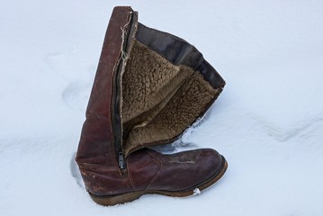 an old and dirty brown leather boot stands in a snowdrift of white snow