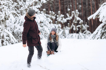 Fototapeta na wymiar Young couple sledding and enjoying outdoors while falling snow