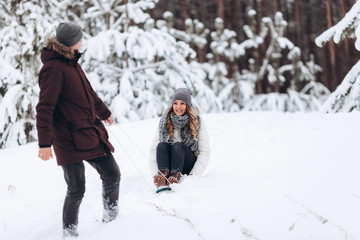 Young couple sledding and enjoying outdoors while falling snow