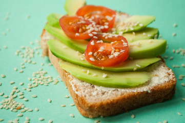 Delicious toasts with sliced avocado, tomatoes and sesamum seeds on blue background with copyspace. Healthy food concept.
