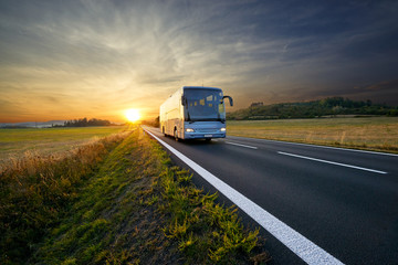 Bus traveling on the asphalt road in rural landscape at sunset