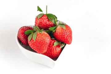 Fresh strawberries in a heart shaped bowl isolated on white background.