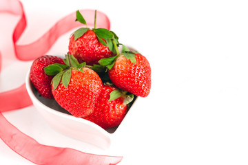 Fresh strawberries in a heart shaped bowl isolated on white background. Valentine Day.