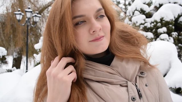 Portrait of a beautiful red-haired young girl in a jacket on the background of snow and pine branches.
