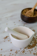 Coriander seeds in porcelain mortar and on white wooden table.