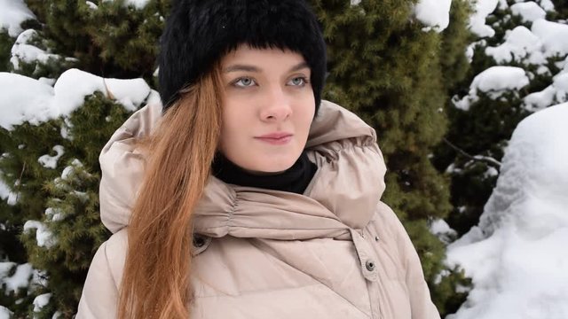 Portrait of a young girl in a black hat on the background of snow branches in winter.