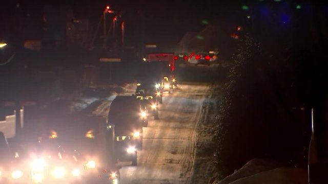 Cars are driving along a snowy road at night. Light glare headlights.