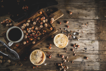 Homemade hazelnut coffee latte or cappuccino, rustic wooden background with hazelnuts, three coffee cups copy space
