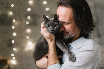 handsome adult man holding a funny gray cat. Breed Russian blue. In the background in the blur lights.