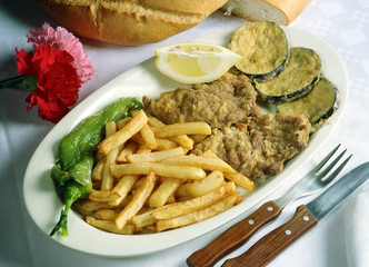 Plato con dos trozos de solomillo de ternera, y berenjenas rebozados, patatas fritas y un pimiento asado.