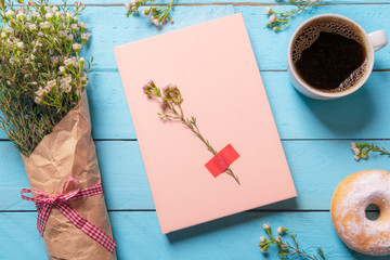 Pink notebook on a wooden table and white flowers bouquet