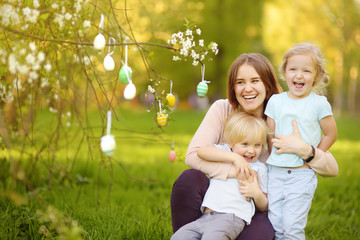 Charming little children with their mother hunting for painted eggs in spring park on Easter day