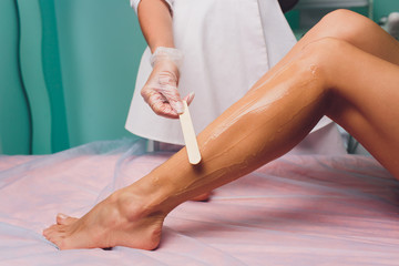 The beautician is preparing for depilation and applying the cream with wax stick on the beautiful...