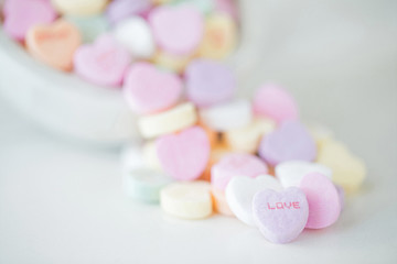 Obraz na płótnie Canvas Valentine photograph of pastel candy hearts pouring out of a glass jar onto a white background