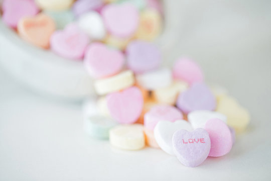Valentine photograph of pastel candy hearts pouring out of a glass jar onto a white background