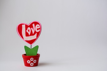 St. Valentine's Day. Red wooden heart with the inscription "love". On a spring in a pot on a white background.