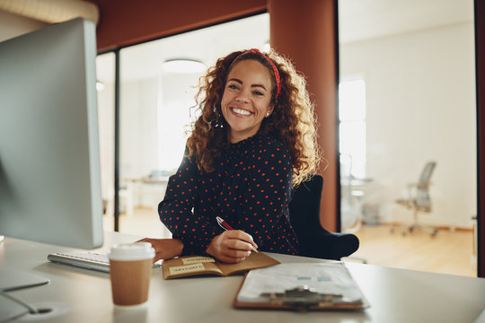 Smiling businesswoman writing down notes while working at her de