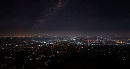 Beautiful super wide-angle night aerial view of Los Angeles, California, USA, with downtown district and mountains with sky full of stars and milky way, seen from the Griffith Park observatory.