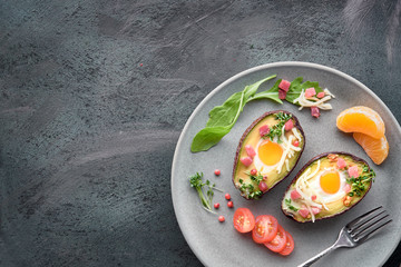 Keto diet dish: Avocado boats with ham cubes, quail eggs, cheese on dark with copy-space