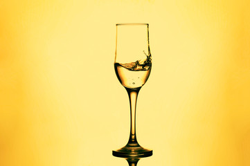 water splash and wine glass. splash alcohol in wine glass on yellow or orange background