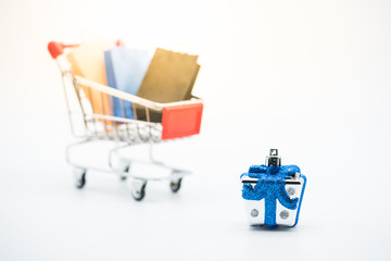 Mini gift box in the red shopping cart filled with shopping bags. Concept of online shopping, festive, unboxing, and Christmas eve and new year sale.