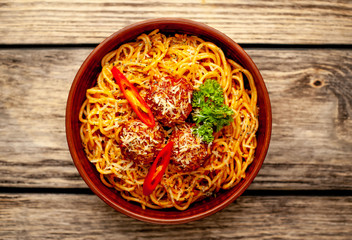 Italian pasta with tomato sauce and meatballs in a plate on a wooden table