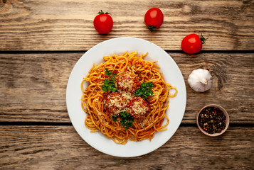 Italian pasta with tomato sauce and meatballs in a plate on a wooden table