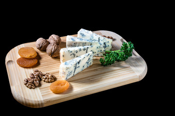 Some peaces of the cheese blue mold roquefort  with dried apricot and peaces of the nuts with parsley at the wooden desk and background