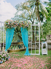 Wedding Arch with pink flowers, petals and blue cloth. Wedding ceremony in Bali.